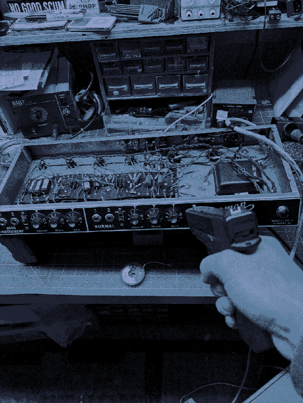 Close-up of a person testing the electronics inside a bass guitar amplifier, with the cover removed, exposing the circuit boards and wiring.