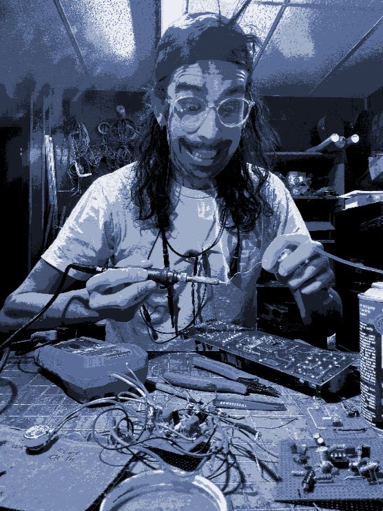 Person working on electronic circuit board with soldering iron in a workshop filled with tools and wires.