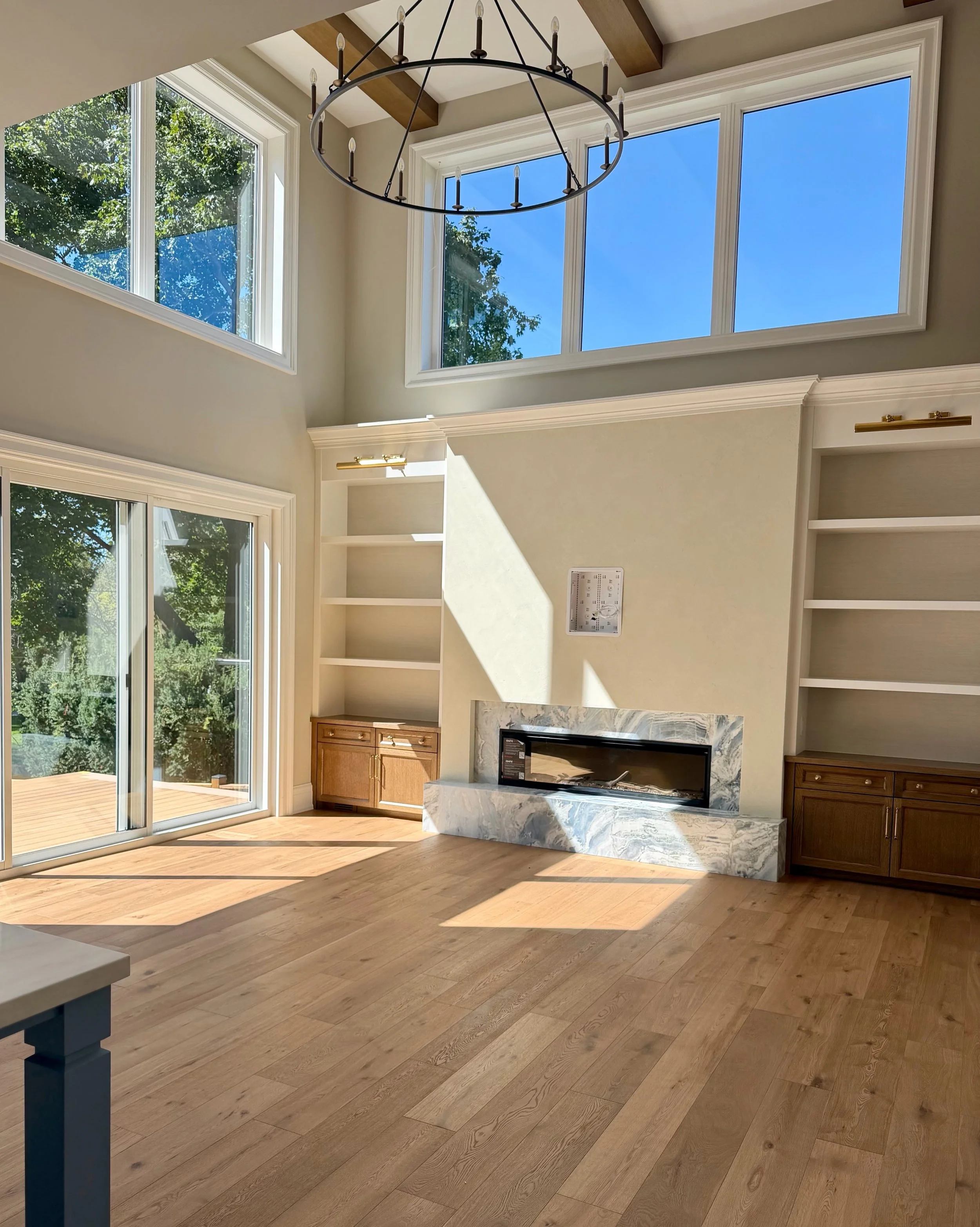 The living room at Maplewood, where volume meets warmth.

Soaring ceilings and expansive windows allow natural light to move through the space, while timber beams, warm oak, and richly veined stone bring it back down to earth. Custom built-ins frame 