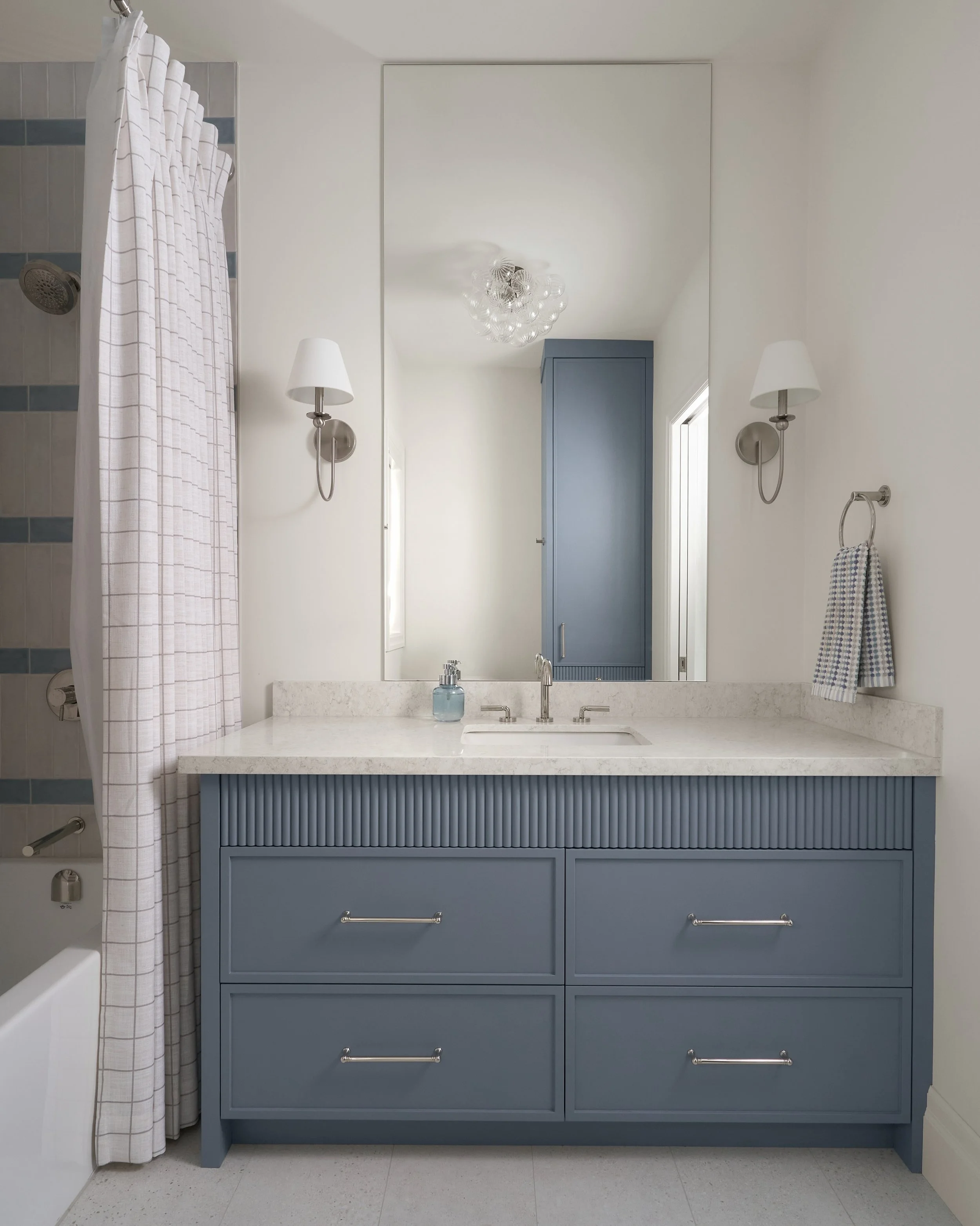 Blue brings a little personality to the everyday.

At Holroyd, a muted blue vanity anchors the bathroom, with fluted detailing that adds texture to the cabinetry. Blue tile stripes carry the colour into the tub surround, balanced by soft neutrals and