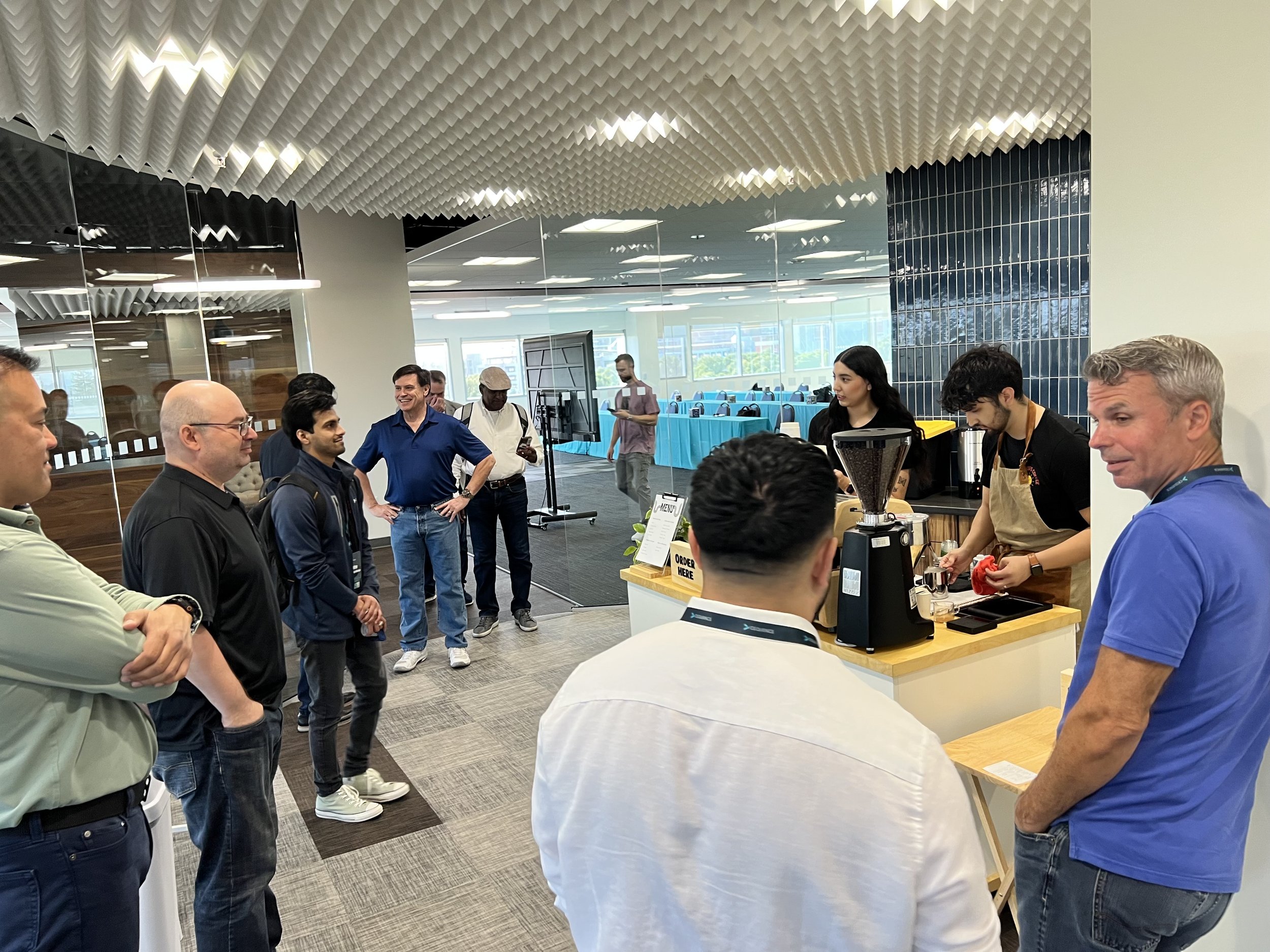 Group of people waiting and a barista preparing coffee at a coffee station in a modern office cafe.