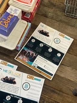 Flyers or brochures about a community or organization, placed on a wooden surface near a bookshelf and a shopping cart.