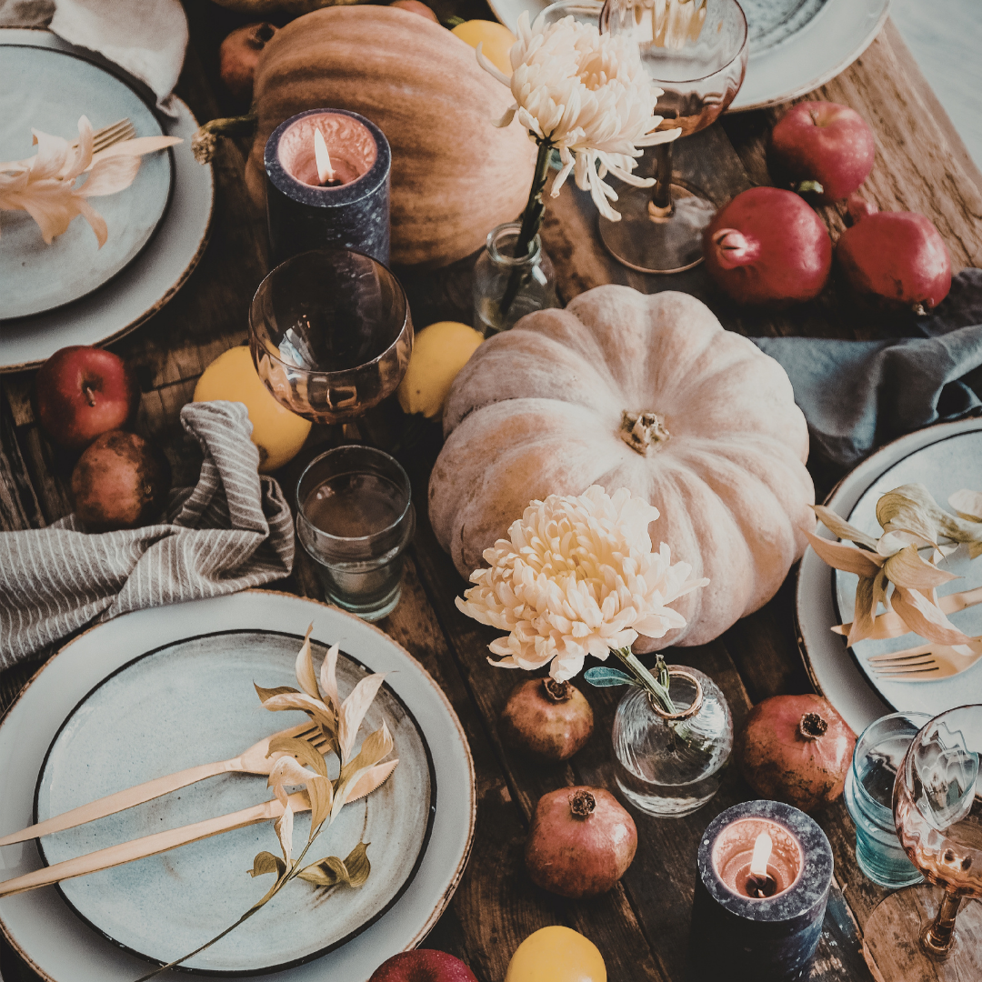 Autumn table settings with gold flatware, amber colored wine glasses, and gold leaves on the table. Pumpkins, apples and pomegranates. Bright flowers adorn the table.