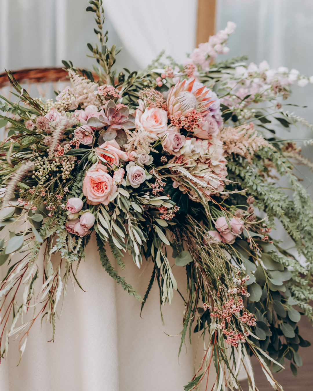 Floral arrangement on head of table for a wedding. Pink roses with olive branches, ferns and lush greenery.