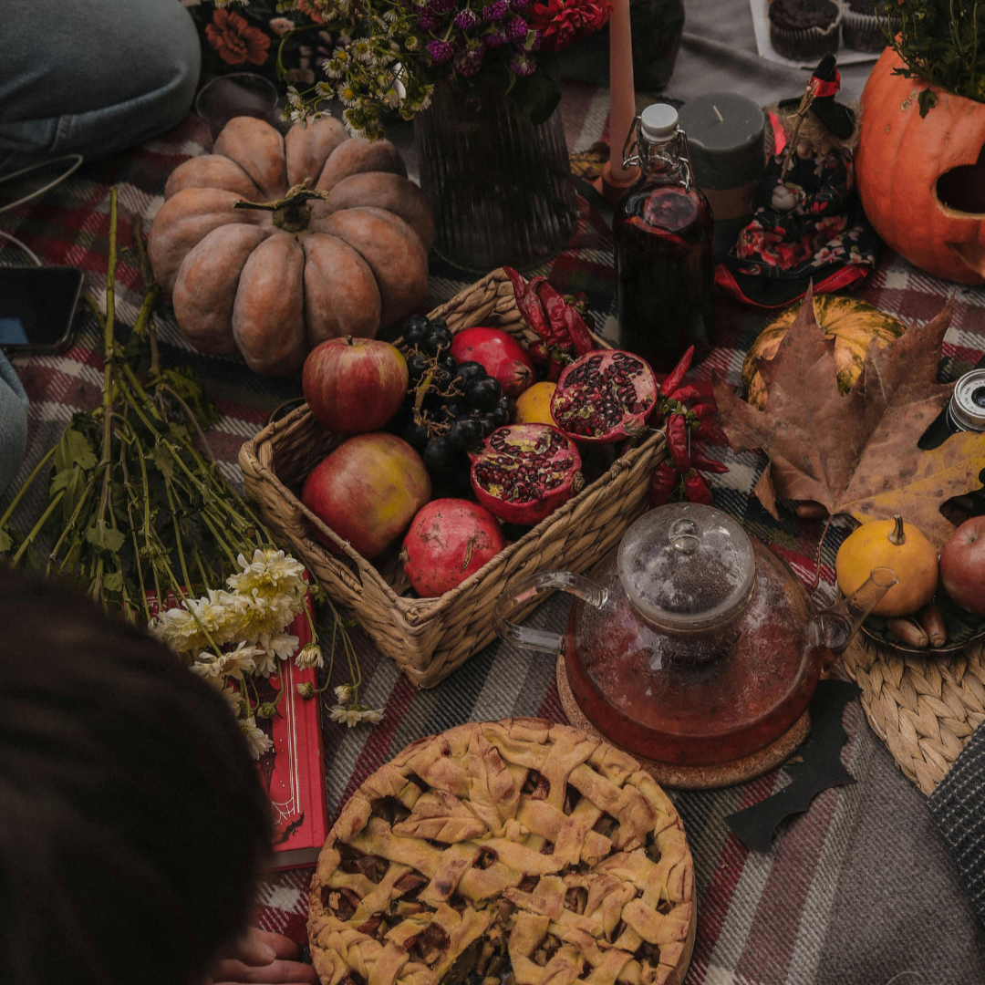 Fall table with pumpkins, apples, pomegranate and cider. A pie lays on the table next to flowers, fall leaves and candles.