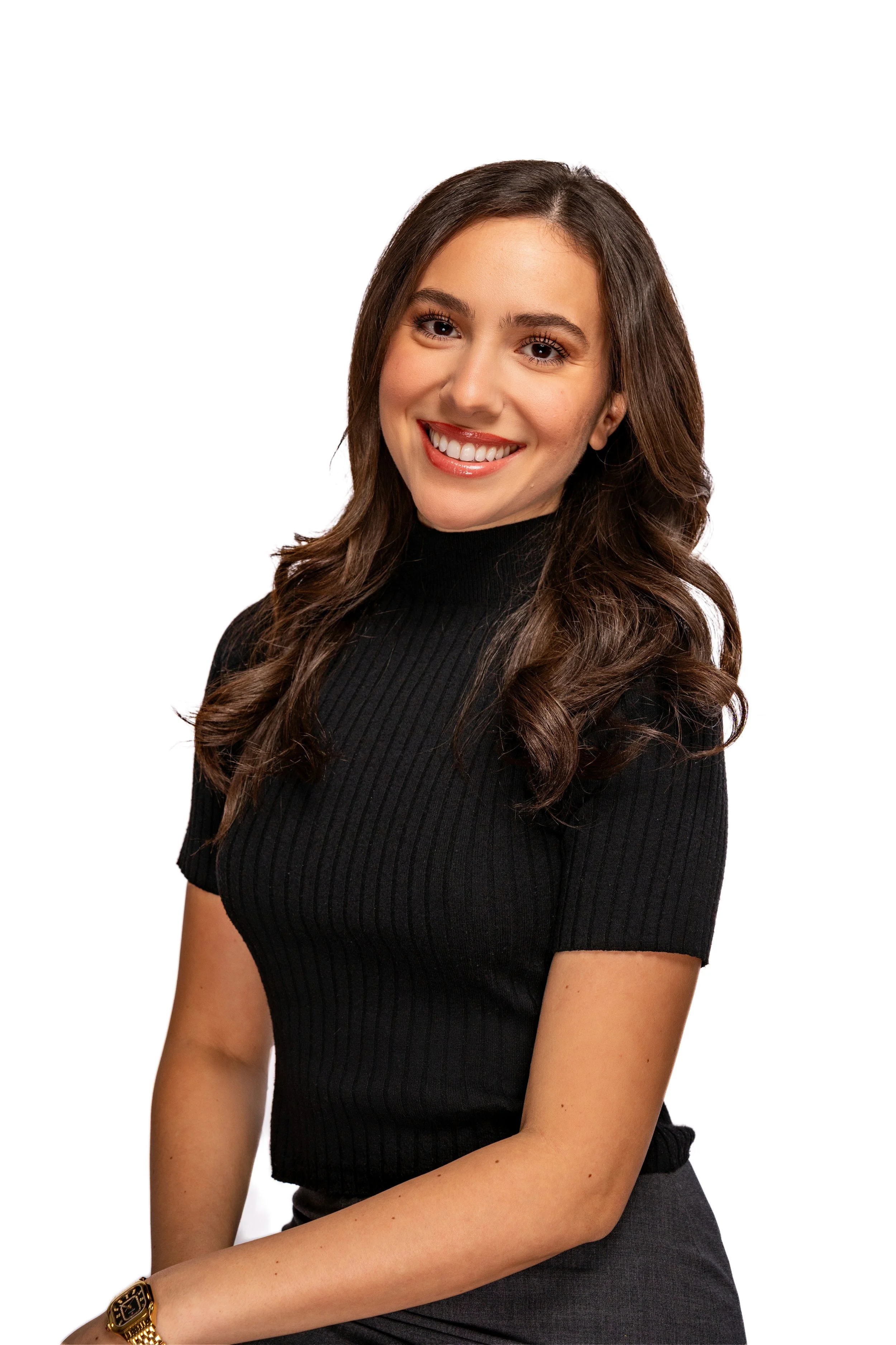 A young woman with long wavy brown hair smiling, wearing a black turtleneck and a gold watch, against a white background.