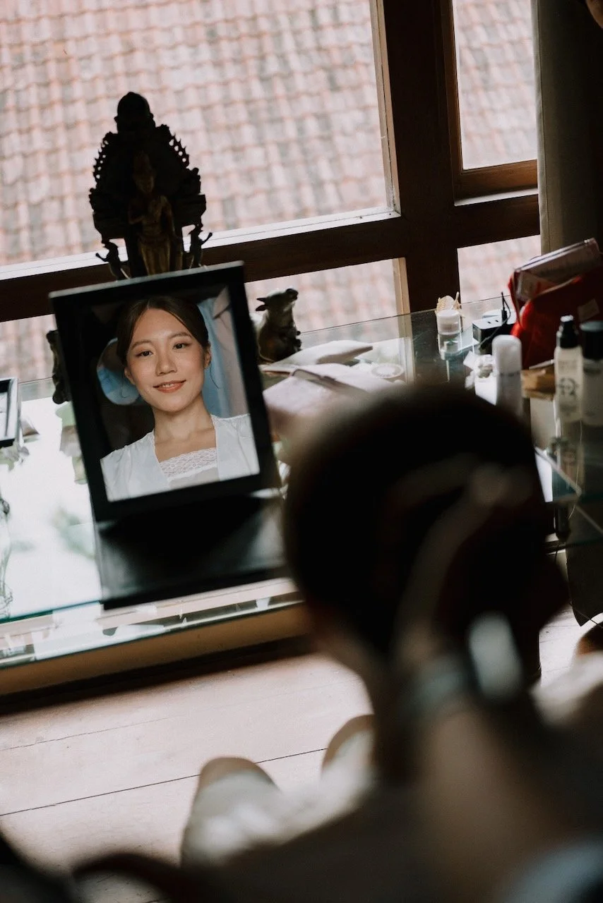 Bride smiling in makeup mirror reflection during wedding morning preparations in Bali villa.