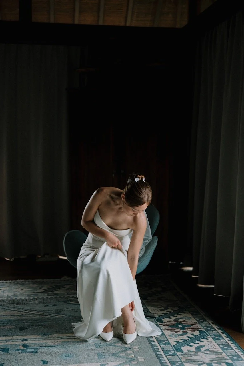 Bride in elegant white gown putting on shoes during quiet bridal preparation at Bali destination wedding.
