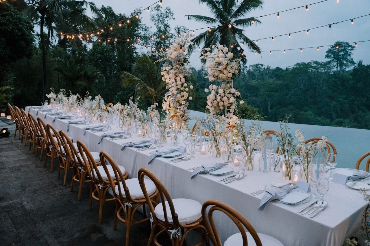 Romantic wedding reception table setup with tall floral arrangements and jungle views by the infinity pool in Bali.