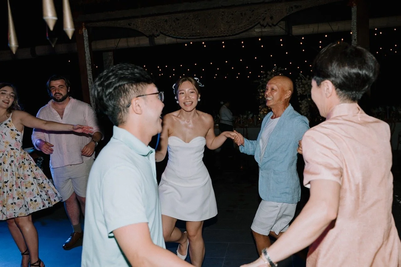 Guests and newlyweds dancing in a circle under night sky lights at lively Bali wedding reception.
