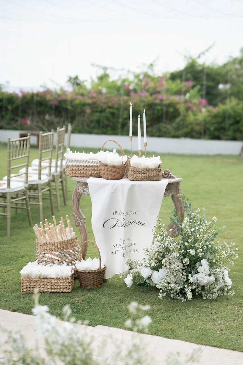 Styled welcome table with petal cones, baskets and florals for guests at an elegant outdoor Bali wedding ceremony.