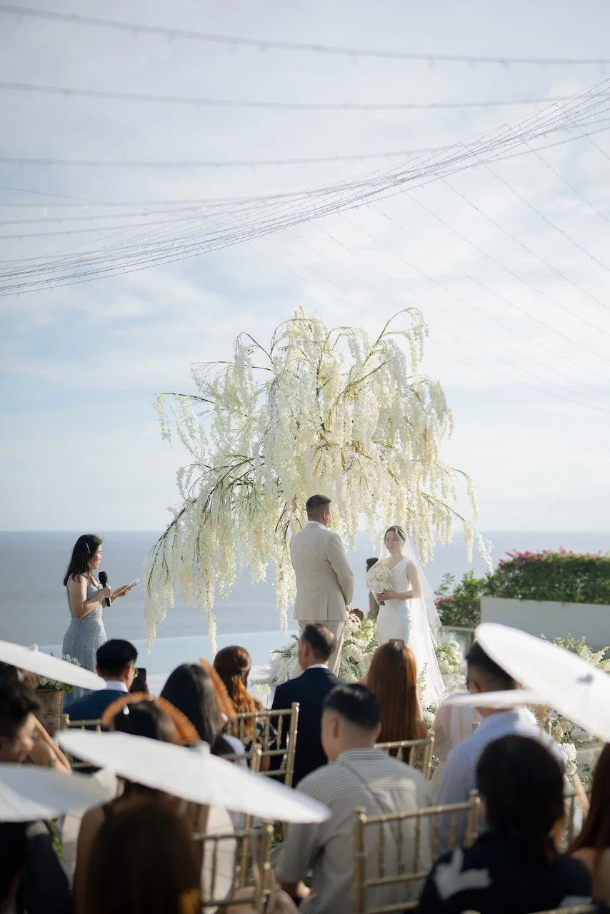 Wide view of an intimate Bali wedding ceremony with guests seated under soft canopy lighting overlooking the ocean.