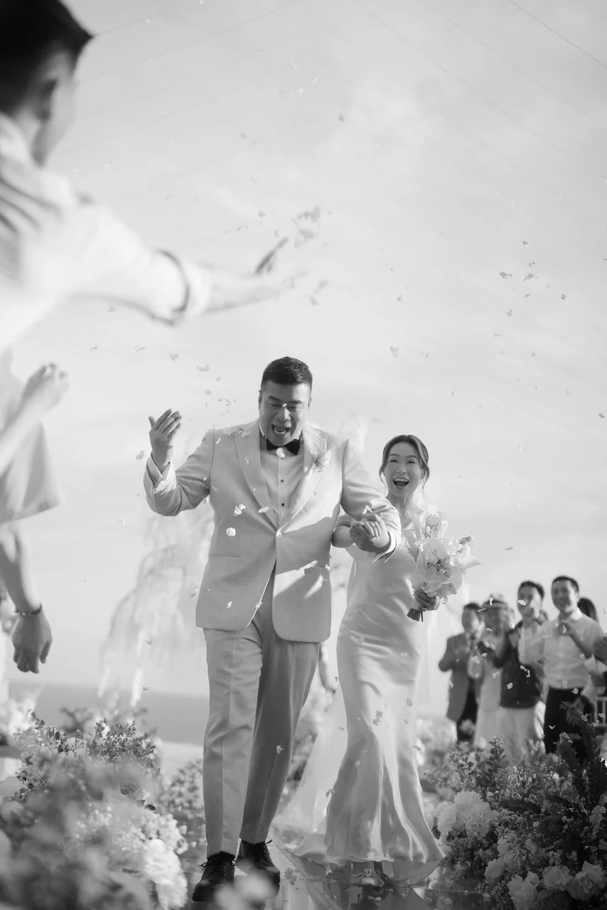 Newlyweds celebrating their aisle exit as flower petals are tossed at a romantic Bali wedding ceremony.