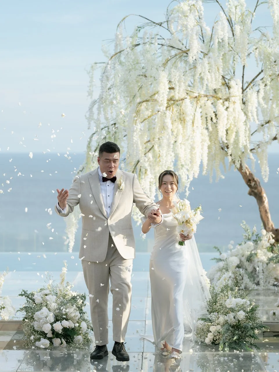 Joyful couple walking back down the aisle beneath a floral ceremony tree at a luxury Bali oceanfront wedding.