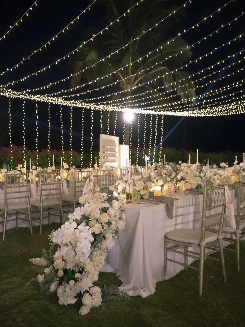 Romantic outdoor wedding reception with long tables, white florals and cascading fairy lights in Bali.
