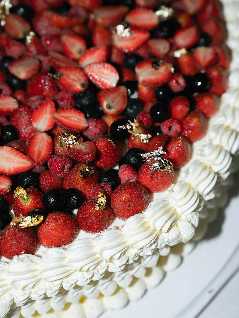 Close-up of elegant wedding cake topped with fresh berries and gold leaf at a Bali wedding celebration.