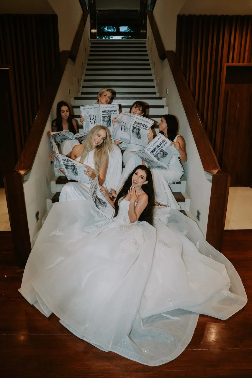 Bride and bridesmaids posing with custom wedding newspapers during a stylish Bali destination wedding celebration