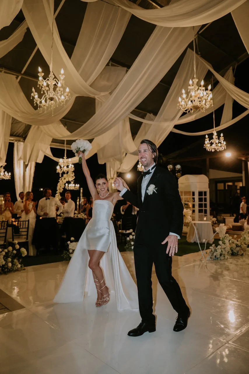 Bride and groom making their reception entrance beneath chandeliers and flowing fabric at their Bali wedding celebration