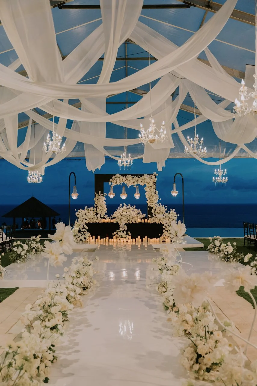 Night-time view of the ceremony space at The Surga Bali with white florals, candles and dramatic draping