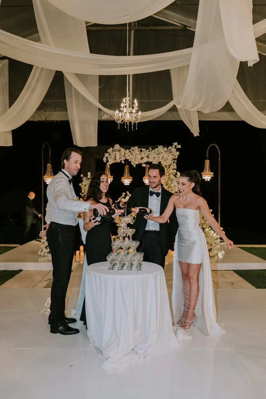 Bride and groom pouring champagne into a glass tower with friends during their Bali wedding celebration