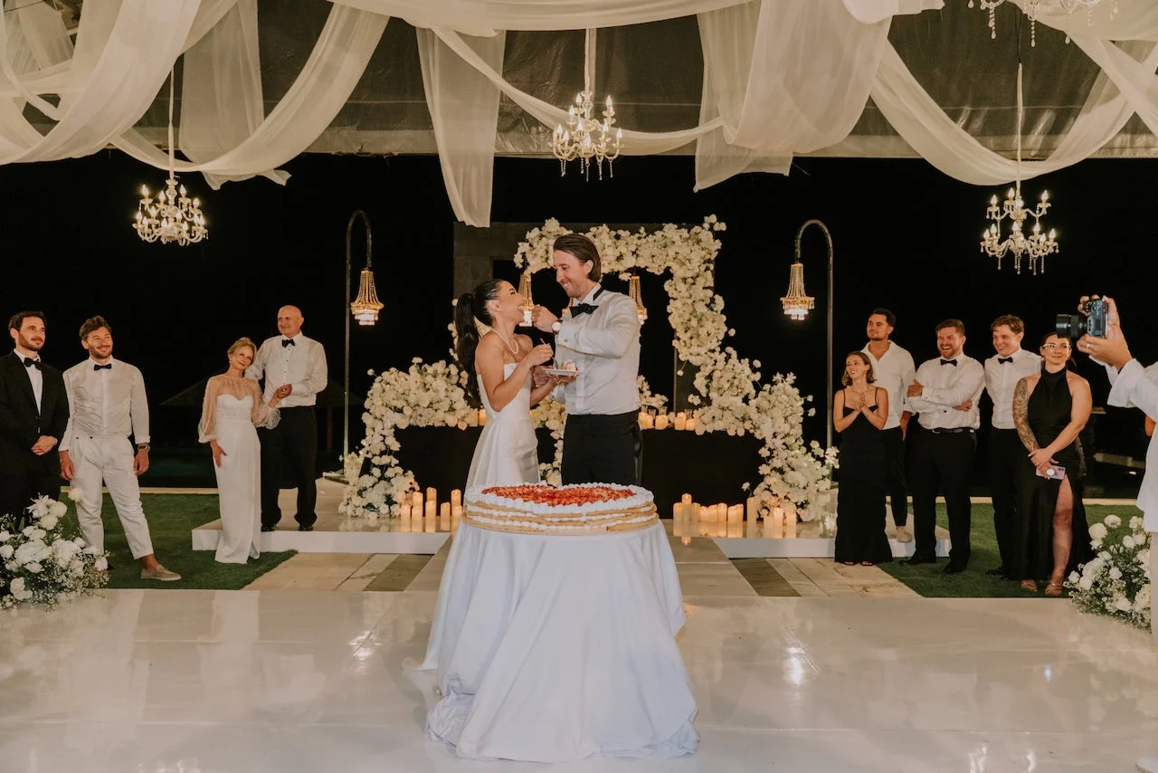 Bride and groom cutting their wedding cake beneath floral installations and chandeliers at a luxury Bali wedding
