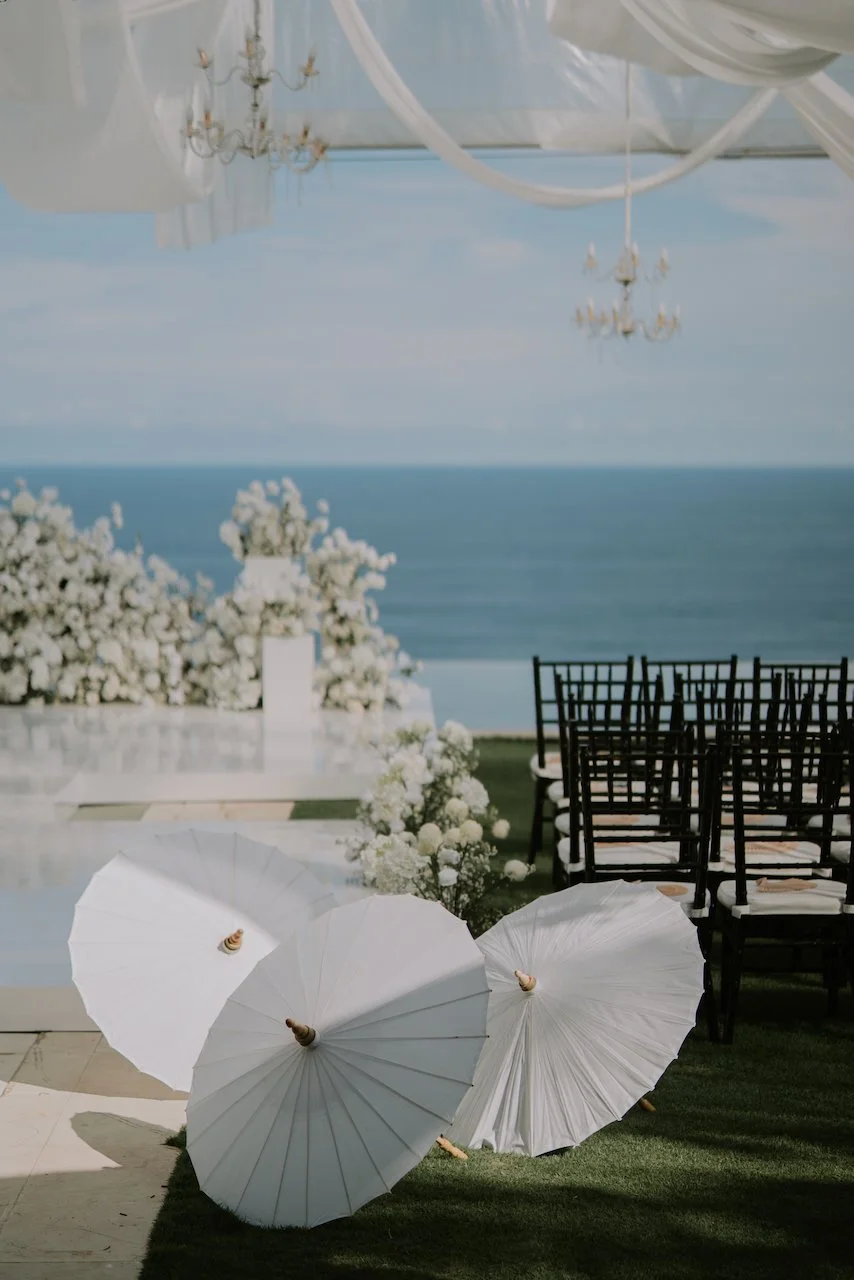 White ceremonial parasols and floral details framing the oceanfront ceremony space at a Bali wedding venue