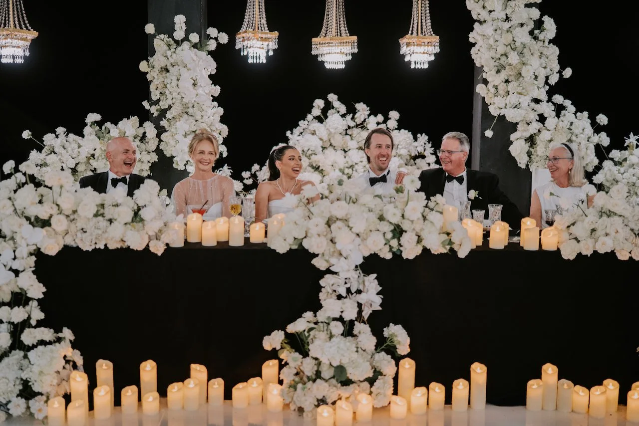 Bride and groom laughing with family at the floral-adorned head table during their Bali wedding reception