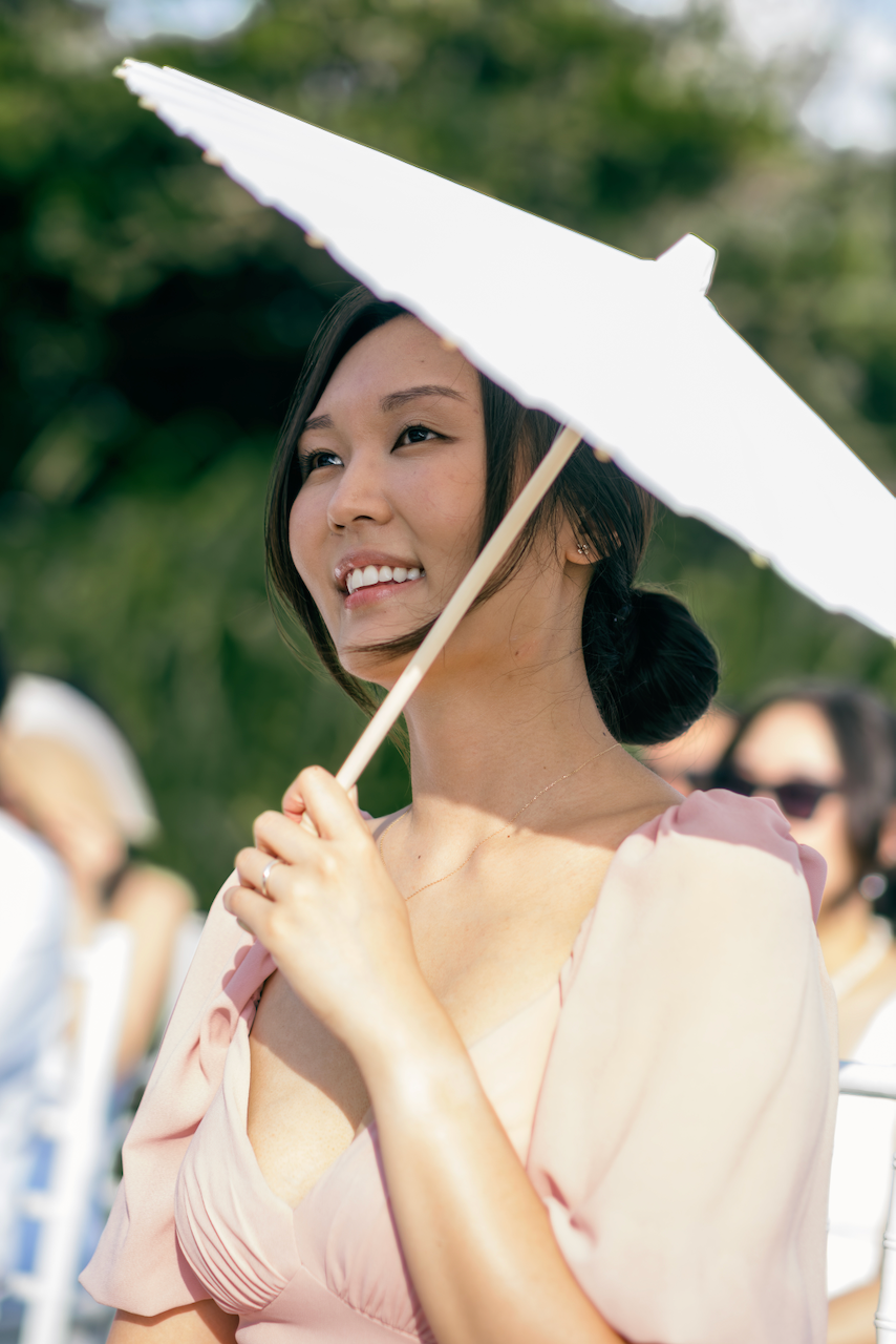 Guest smiling under a white paper parasol at a sunny outdoor tropical ceremony