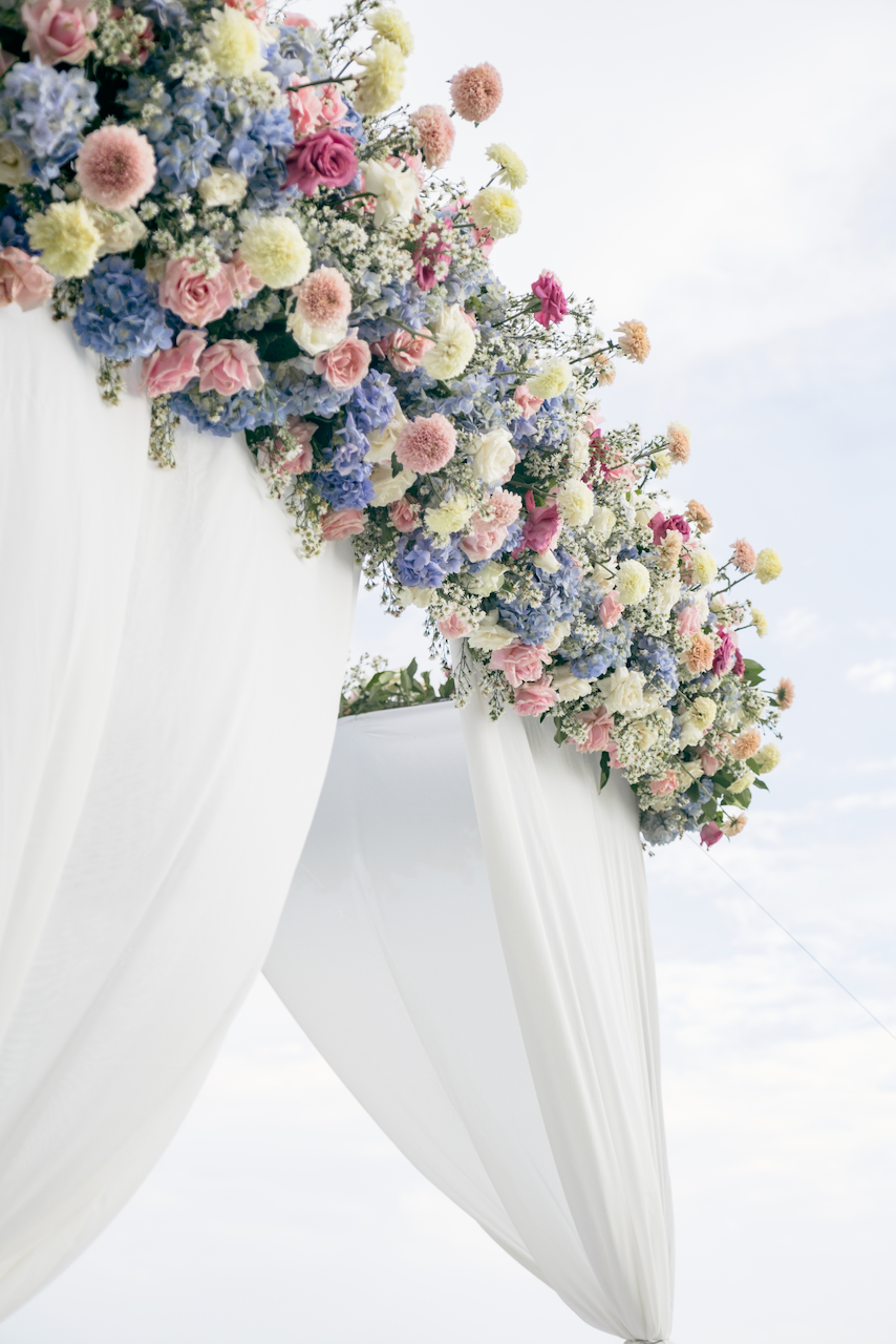 Romantic Bali wedding ceremony arch decorated with lush pastel floral arrangements and white draping