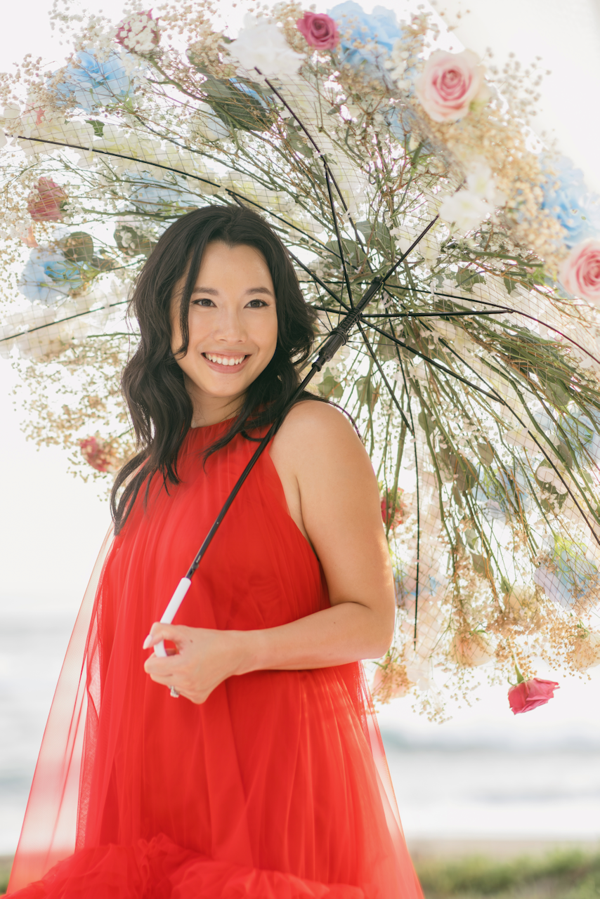 Radiant bride in a vibrant red tulle dress holding a custom flower umbrella