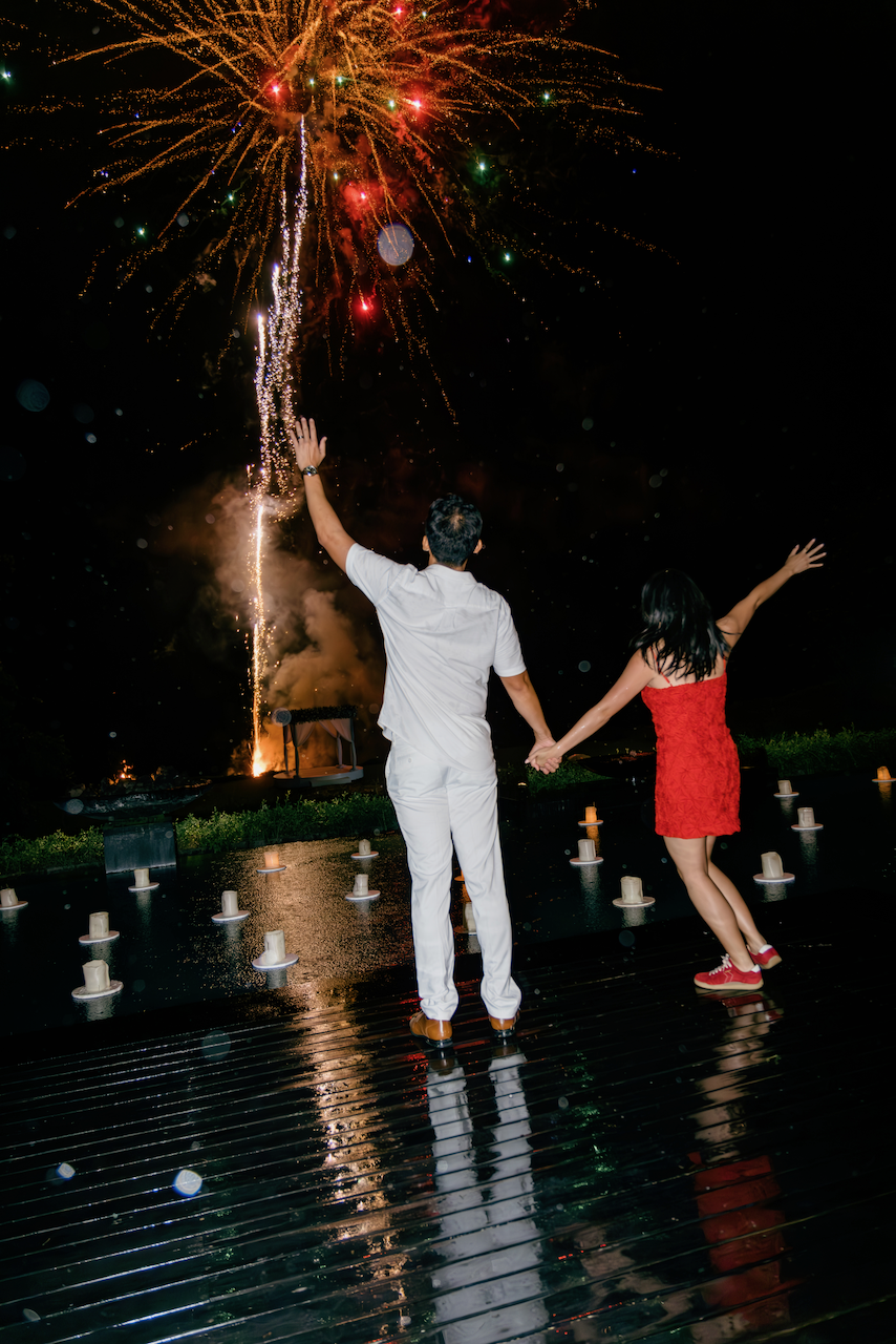 Newlyweds holding hands and watching a spectacular fireworks display over the water in Bali