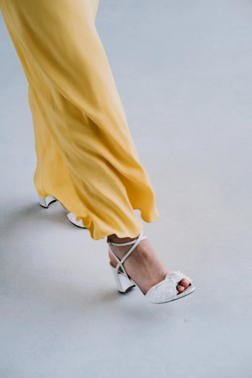 Close-up of a bridesmaid stepping in a yellow gown and chic white pearl block heels.