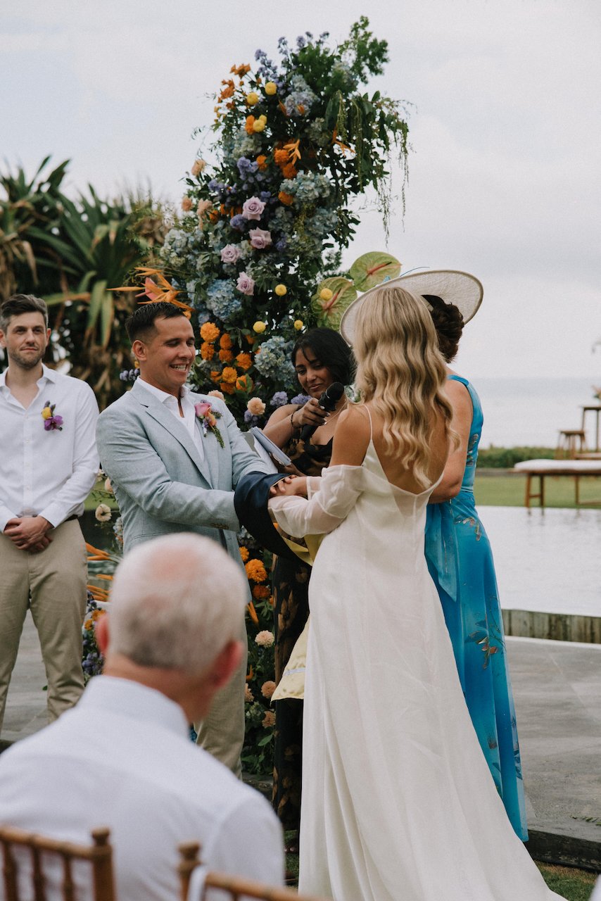 Couple holding hands and exchanging vows before a stunning colorful floral arch at Villa Phalosa.