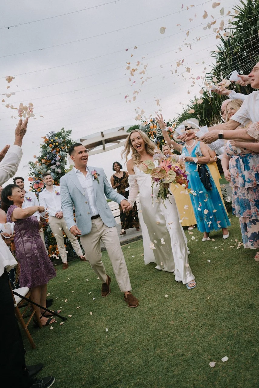 Joyful newlyweds laughing as they walk down the aisle during a romantic flower petal toss.