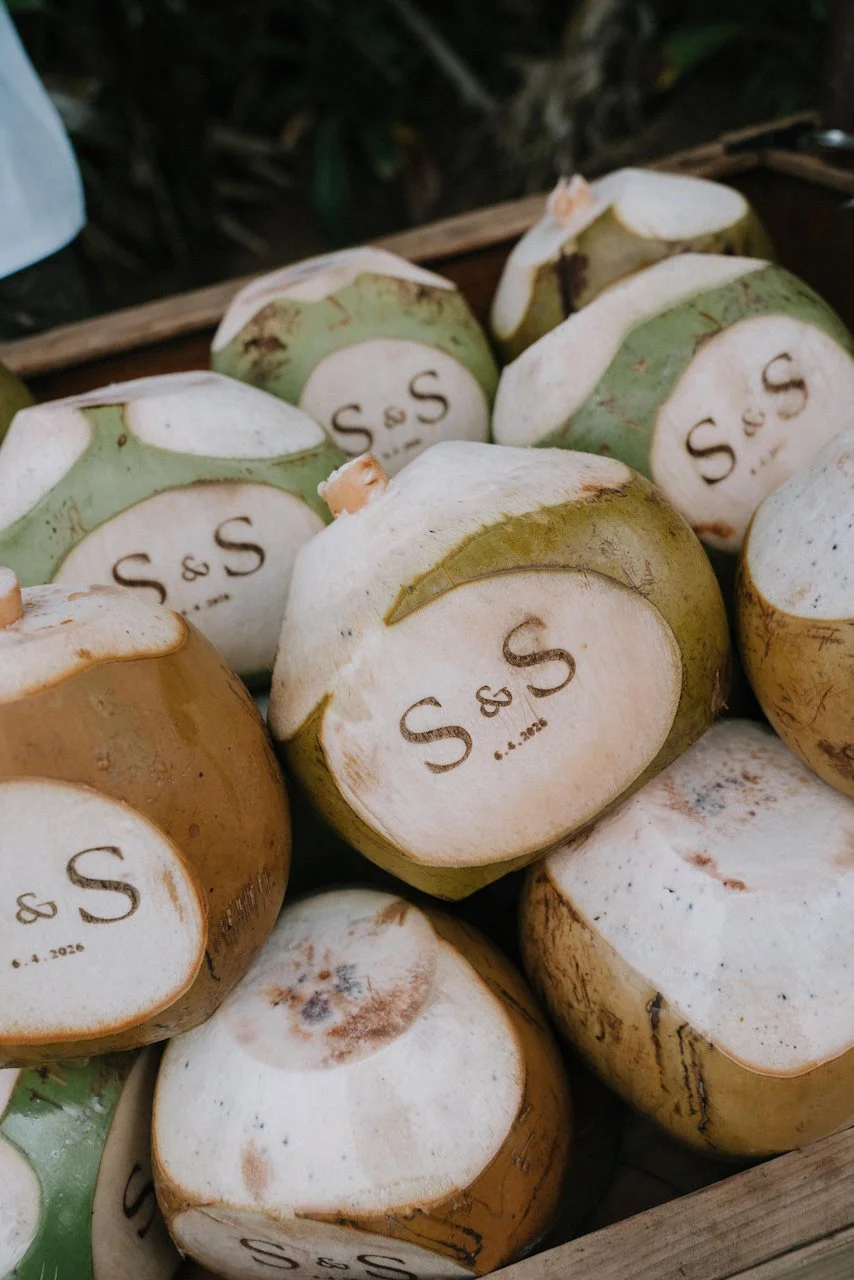 Pile of fresh green coconuts custom engraved with the couple's initials for island wedding guests.