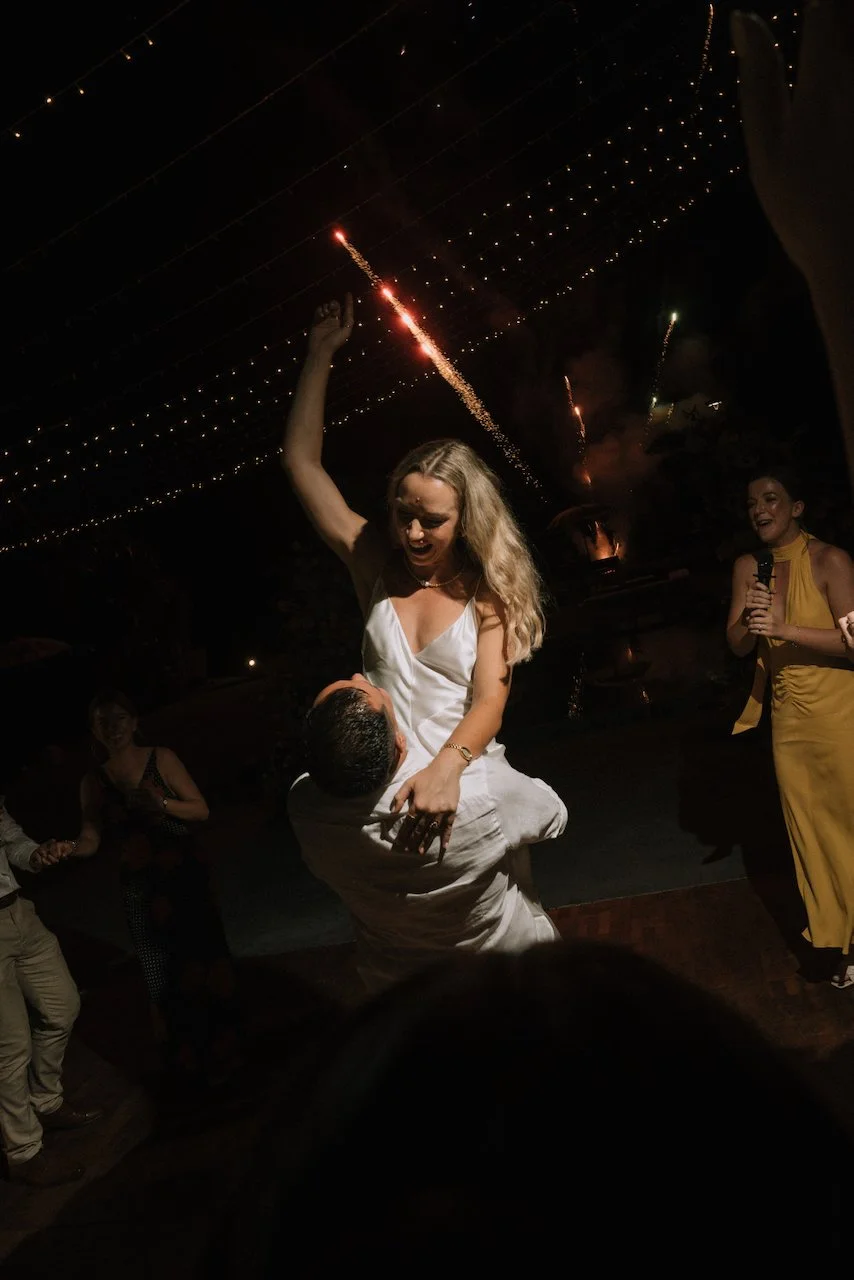 Groom lifting the cheering bride on the dance floor with celebratory fireworks at their Villa Phalosa reception.