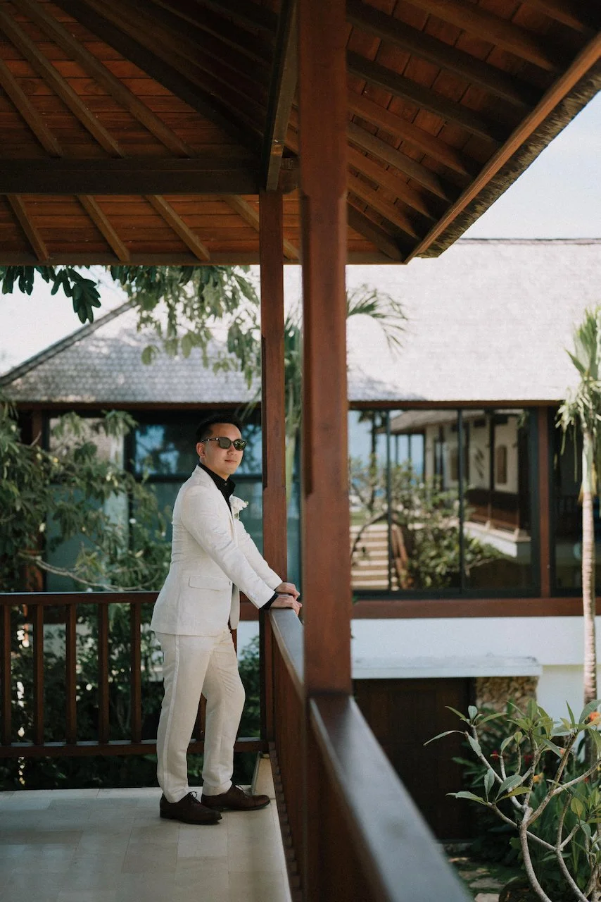 Groom in a stylish white suit relaxing on a wooden balcony at Villa Plenilunio.