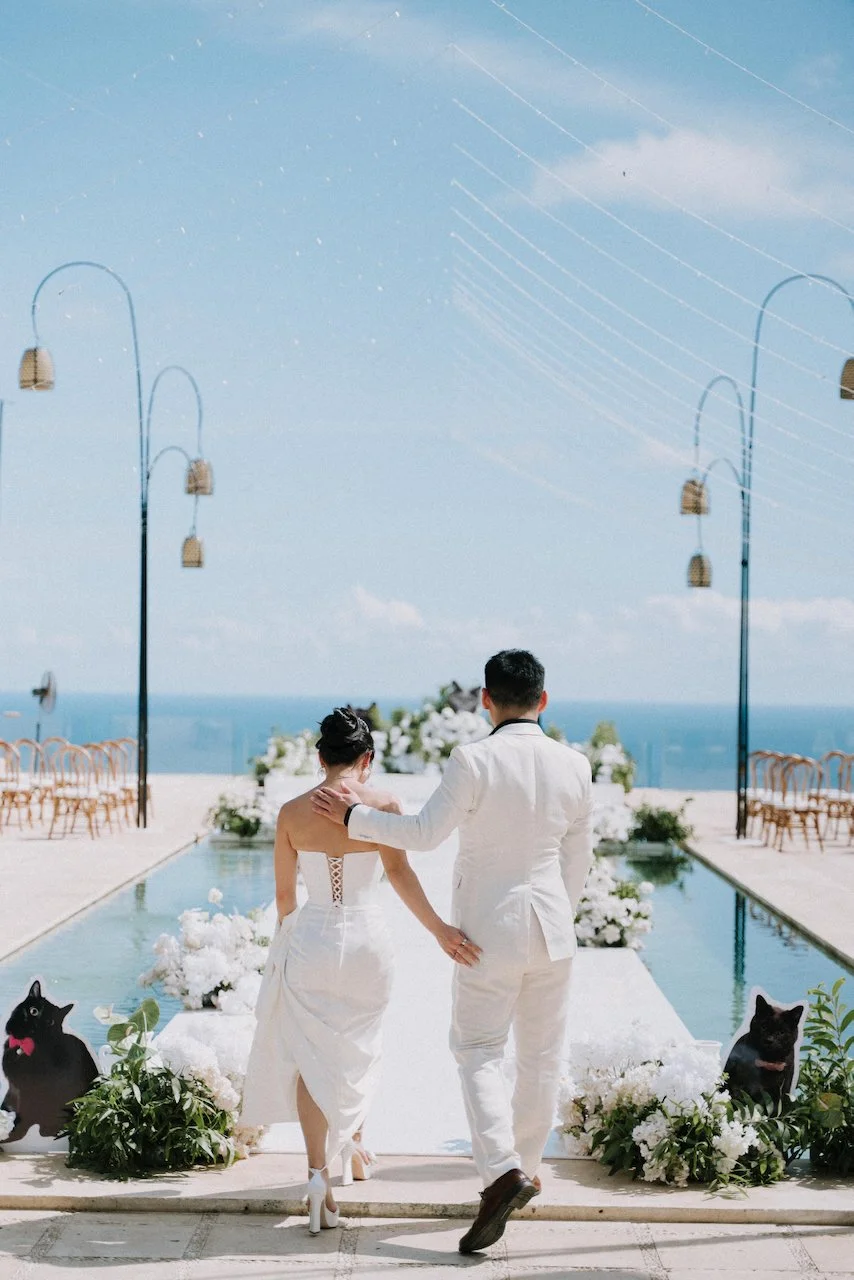 Bride and groom walking down a floating over-pool aisle decorated with playful cat cutouts.