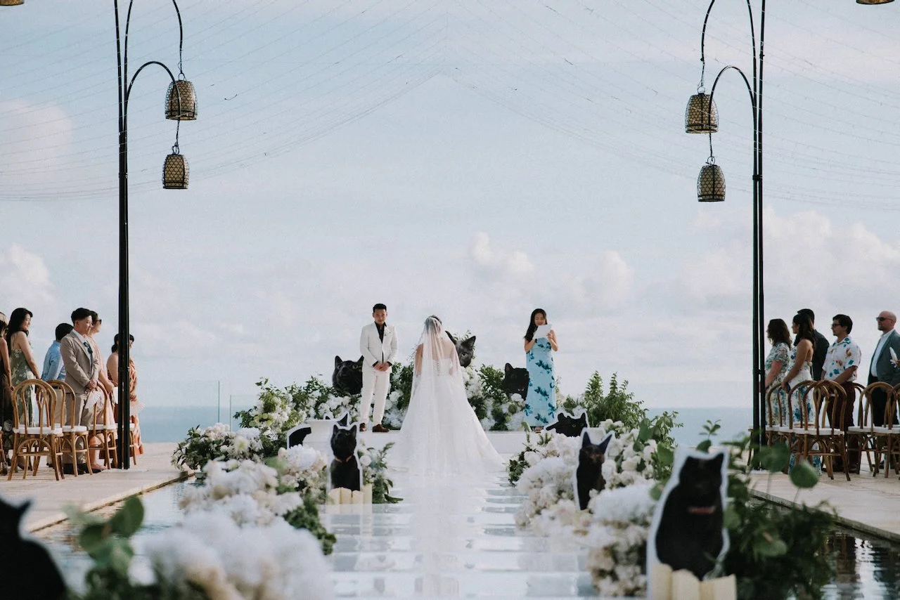 Wide view of an oceanfront wedding ceremony at Villa Plenilunio featuring a mirrored over-pool aisle.