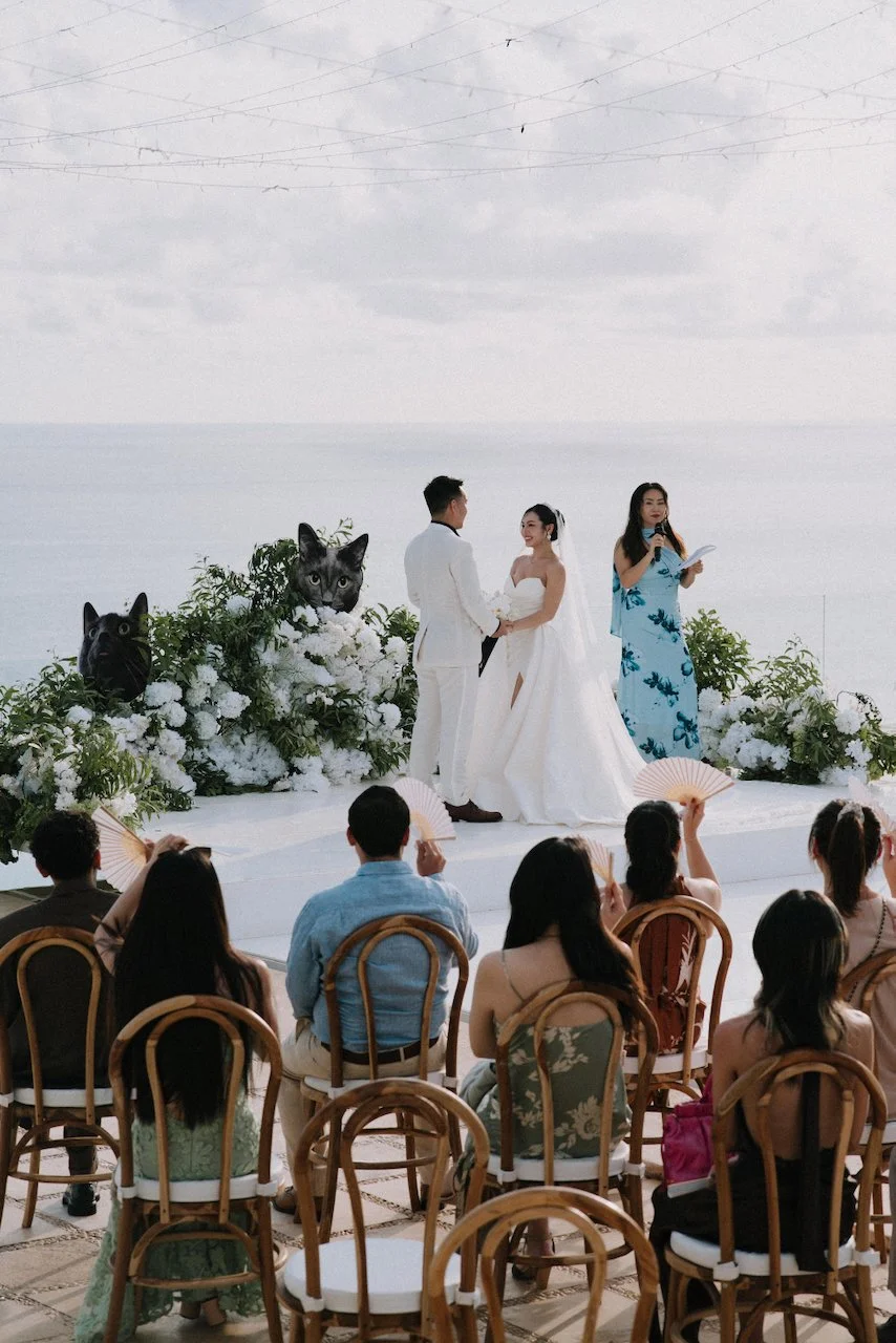 Bride and groom exchanging vows at a floral altar with playful black cat cutouts in Bali.