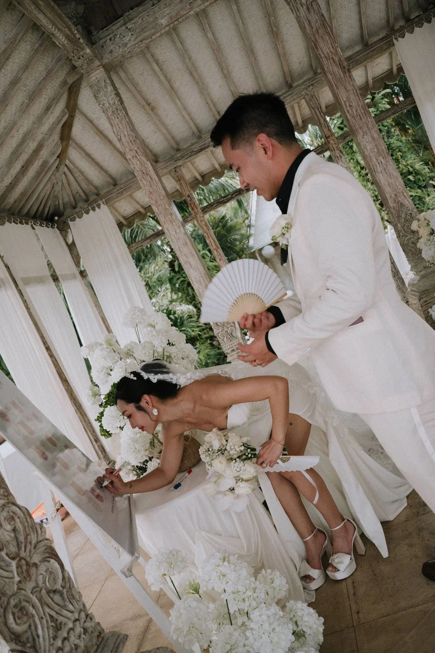 Bride signs a bespoke guest board under a traditional wooden pavilion at the wedding reception.