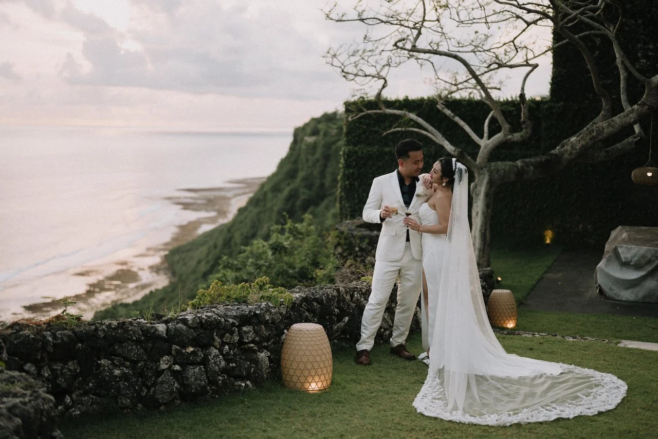Romantic sunset wedding portrait of the bride and groom on a lush cliff overlooking the ocean.