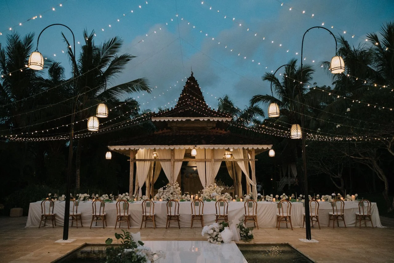Stunning outdoor wedding reception dinner setup under fairy lights and a traditional Balinese pavilion at Villa Plenilunio.