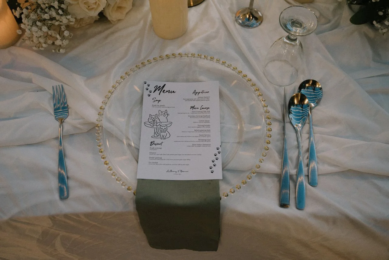 Custom cat-themed wedding menu card resting on a glass beaded charger plate at an elegant table setting.