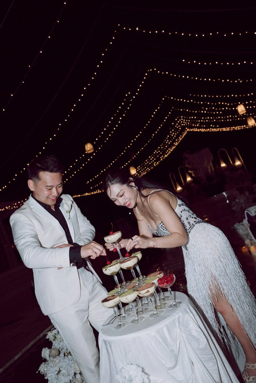 Newlyweds adding fresh cherries to their unique tiramisu dessert tower during their Uluwatu wedding reception.