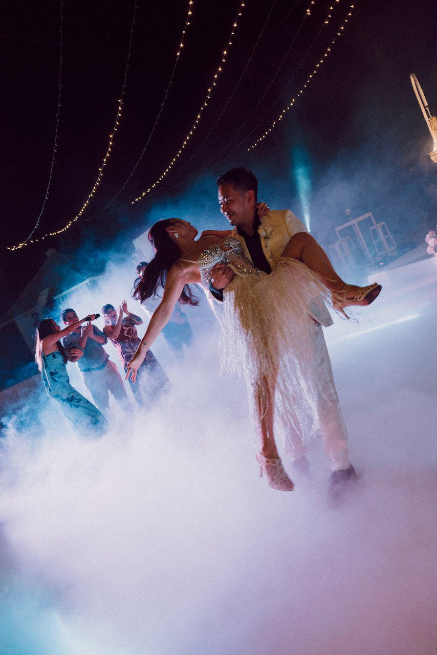 Groom lifting the bride in her sparkly fringe party dress during a dramatic misty first dance.