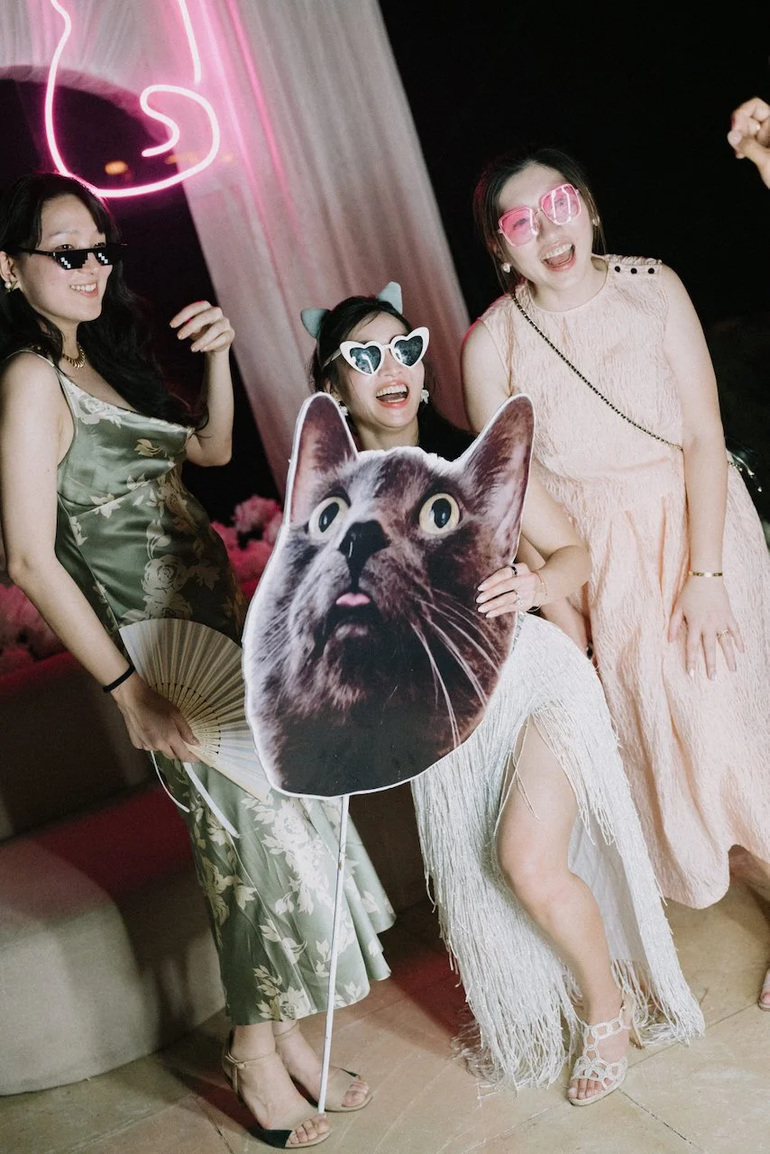 Bride and friends partying on the dance floor with a giant cat face prop and fun sunglasses.