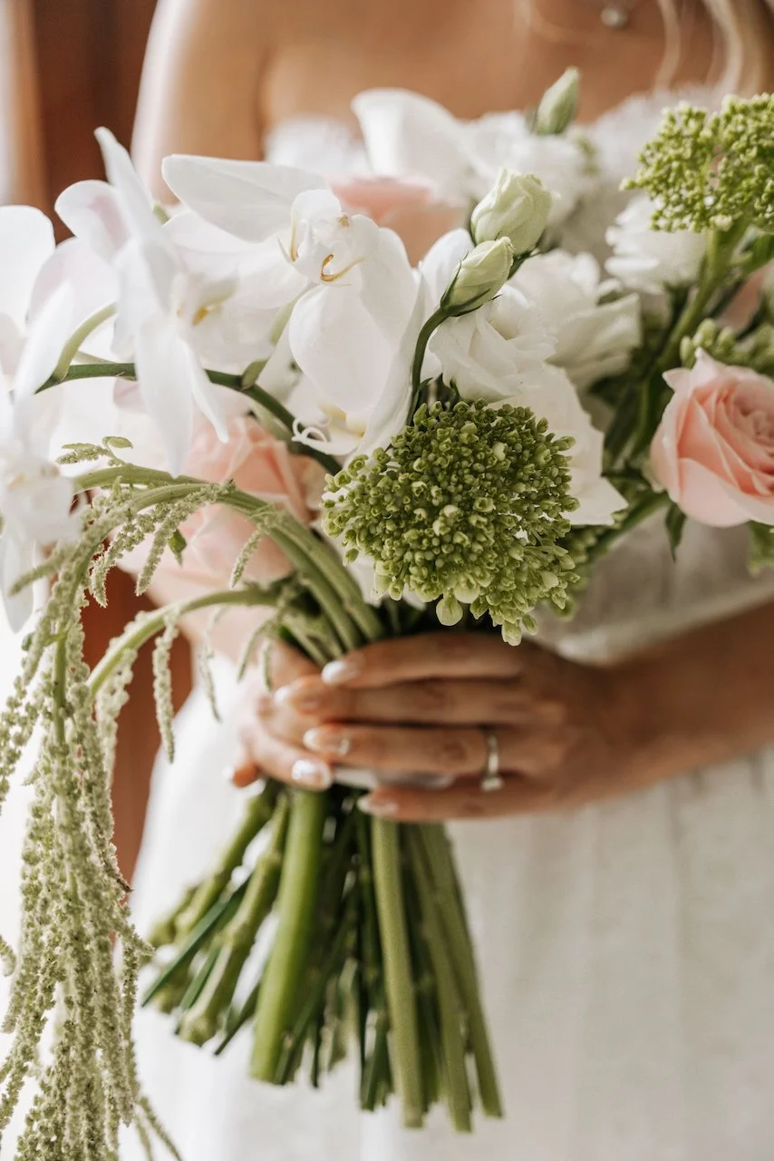 Close-up of an elegant bridal bouquet featuring white orchids, pink roses, and green amaranthus.