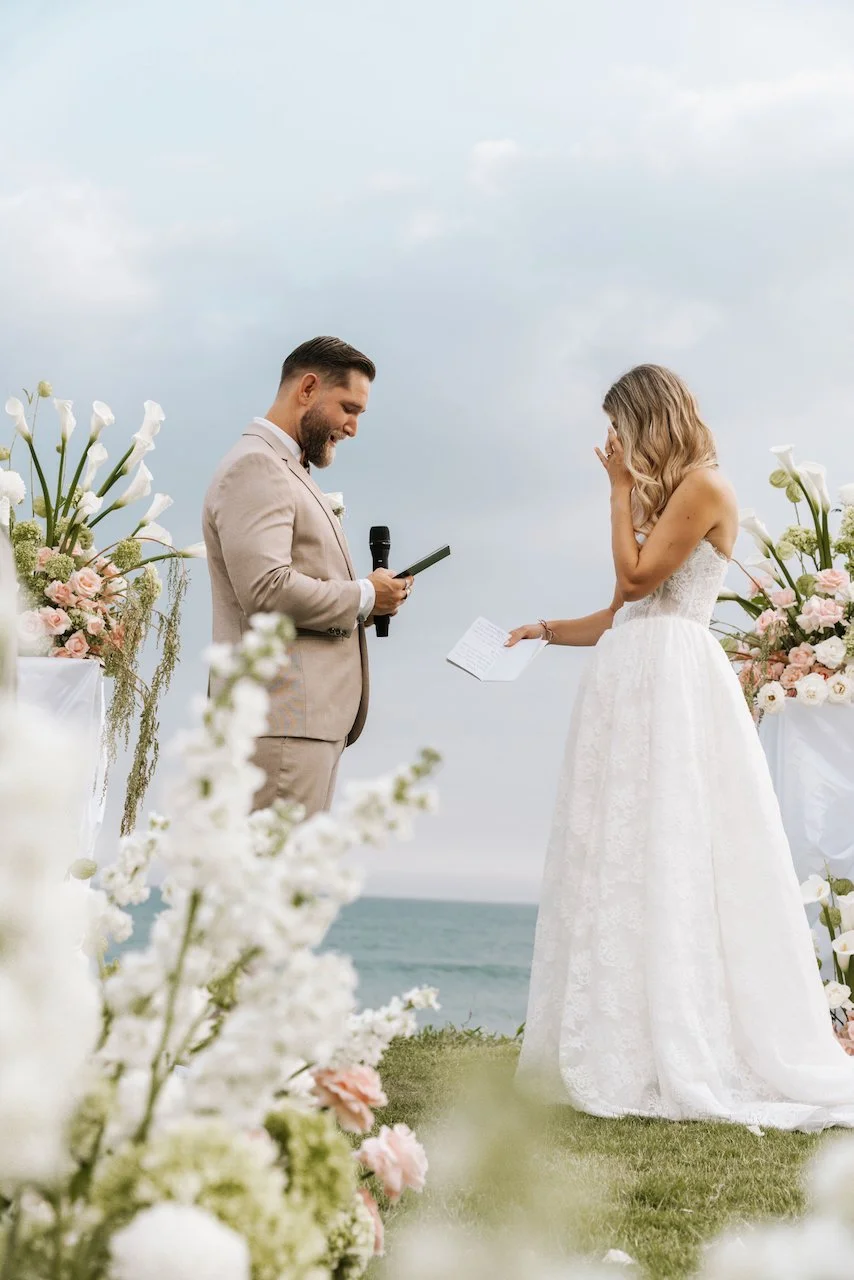 Bride wiping a happy tear during an outdoor cliffside wedding ceremony by the ocean.