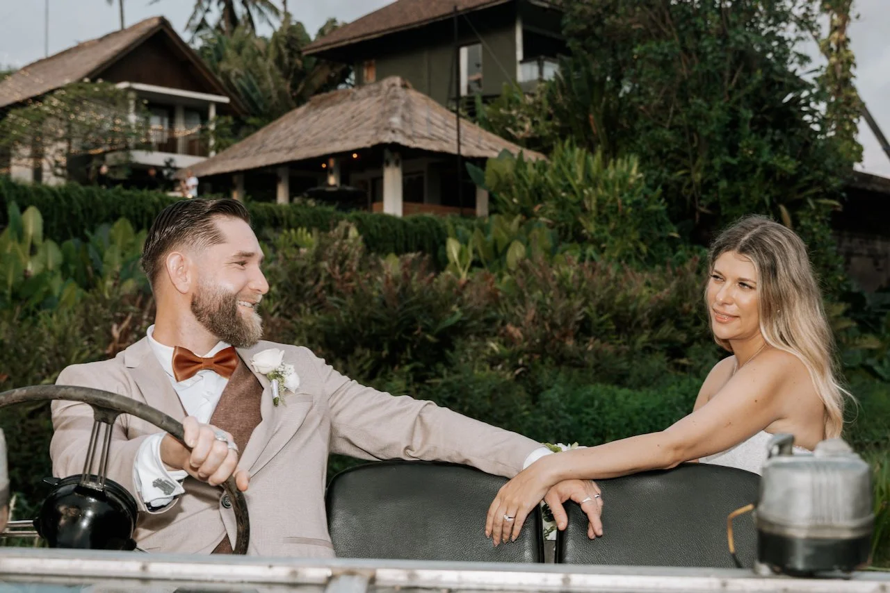 Newlywed couple smiling at each other inside a vintage blue Land Rover.